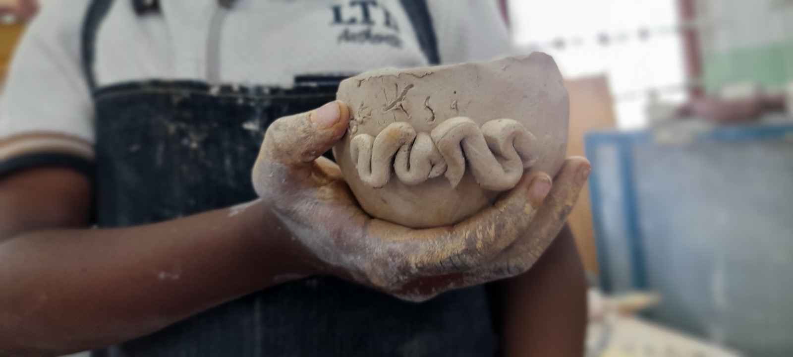 A child holds a handmade clay bowl with raised lettering